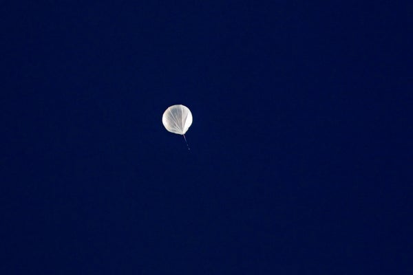 White weather balloon floating against dark blue sky