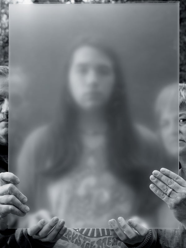 A teenager standing behind a blurry glass with their parents.