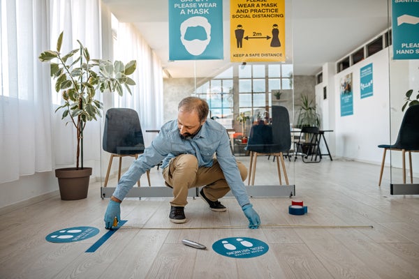 Man measuring and applying social distancing sign on reopening at office.